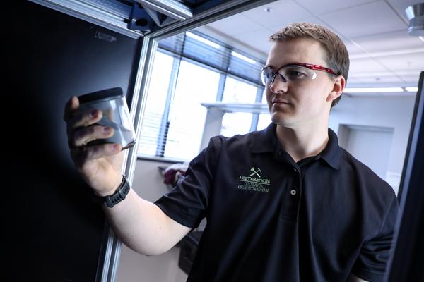 Student wearing safety glasses holding a jar in a 机械 engineering lab